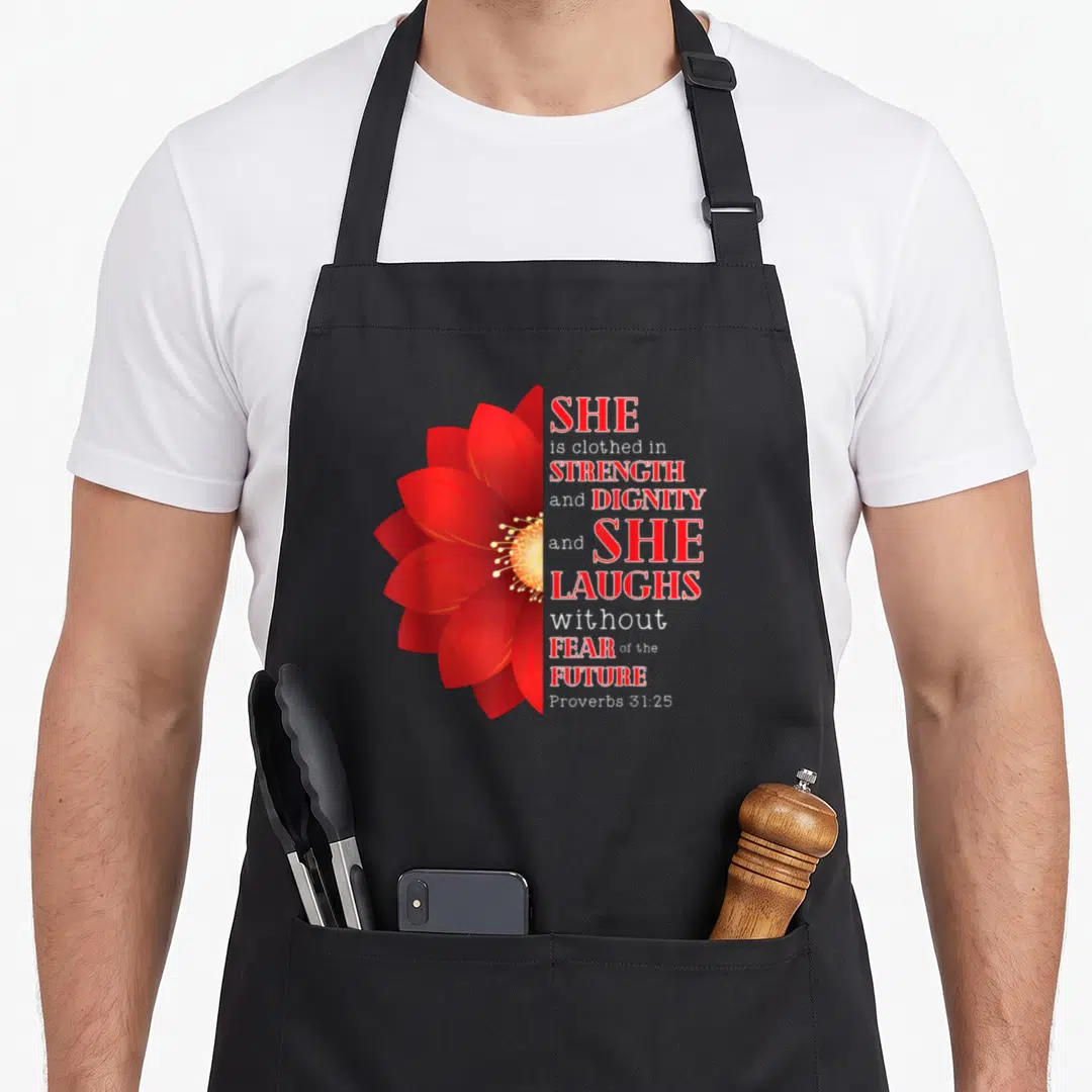 She proverbs apron - Red flower next to stacked text SHE is clothed in STRENGTH and DIGNITY — shown on a black cotton canvas apron against a white background