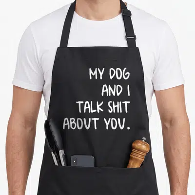 Retro talk dog apron - White stacked text reading MY DOG AND I TALK SHIT ABOUT YOU on black background — shown on a black cotton canvas apron against a white background