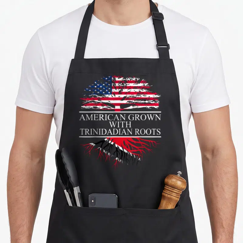 Trinidadian class life apron - Tree with US flag canopy and Trinidad flag roots separating three lines of text — shown on a black cotton canvas apron against a white background