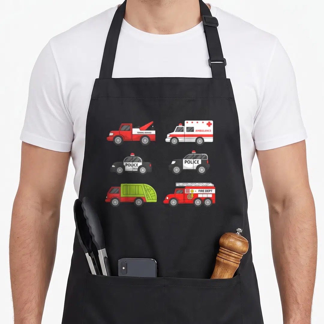 Emergency truck apron - Six cartoon emergency vehicles with TOWING SERVICE AMBULANCE POLICE 911 FIRE DEPT text in red — shown on a black cotton canvas apron against a white background