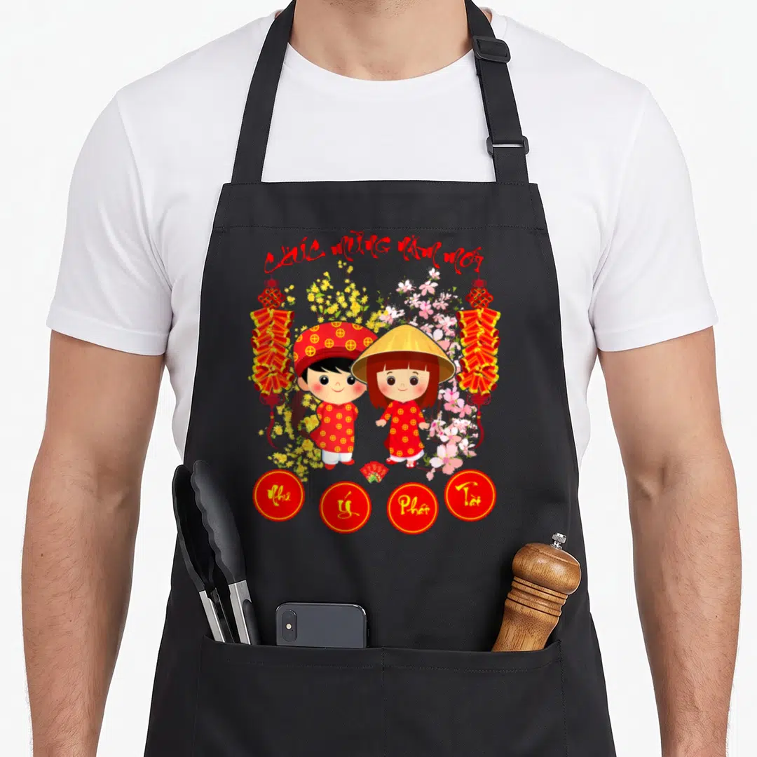Chuc lunar new year apron - Two cartoon children in red robes flanked by yellow pink flowers and four red lucky circles — shown on a black cotton canvas apron against a white background