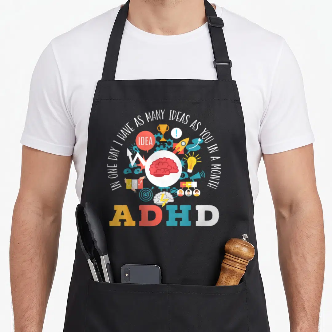 Warrior adhd apron - Red brain in white circle surrounded by icons and text about having many ideas — shown on a black cotton canvas apron against a white background