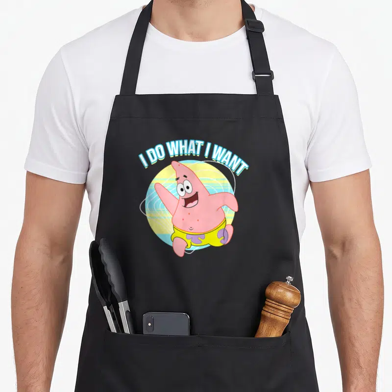 Novelty apron for baking for dad - I DO WHAT I WANT text over pink starfish on yellow and blue circle — shown on a black cotton canvas apron against a white background