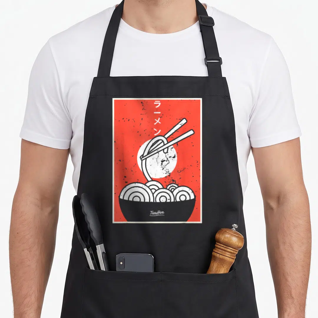 Ramen thai girl apron - Red background with grey ramen bowl, white sun, chopsticks lifting noodles, vertical Japanese — shown on a black cotton canvas apron against a white background