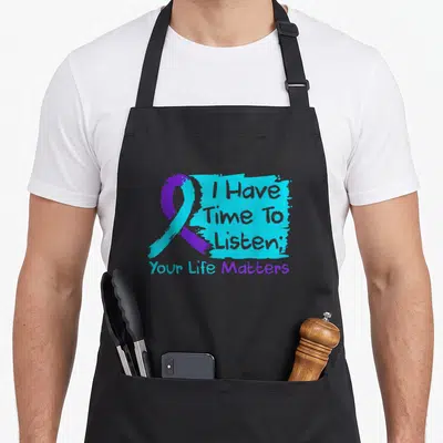 Listen suicide prevention apron - Purple and teal awareness ribbon beside stacked text on teal paint stroke with Your — shown on a black cotton canvas apron against a white background