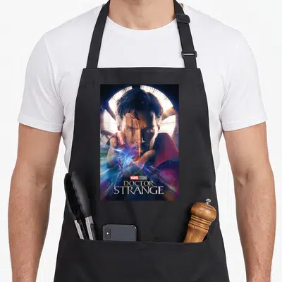 Studio doctor apron - Photo of Doctor Strange with circular window and stacked movie title text — shown on a black cotton canvas apron against a white background