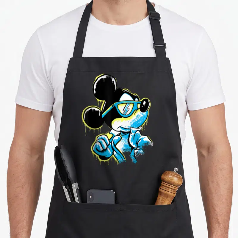 Icy drip apron - Stylized Mickey Mouse in blue sunglasses with yellow paint drip effects on black ears — shown on a black cotton canvas apron against a white background