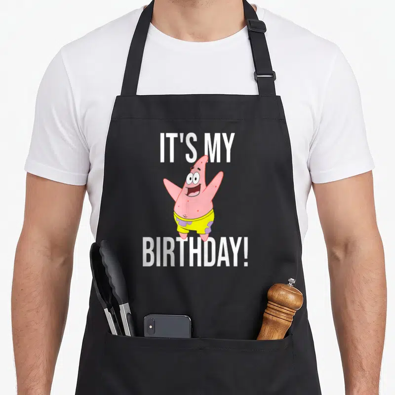 Funny occasion birthday apron - Patrick Star character between IT'S MY BIRTHDAY! text in pink and yellow — shown on a black cotton canvas apron against a white background