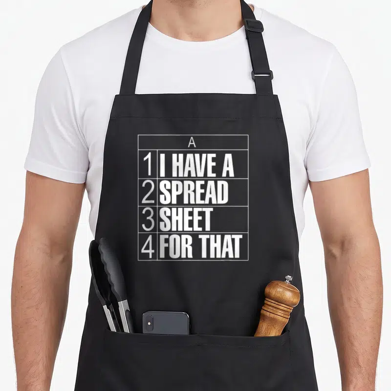 Spreadsheet tax apron - White grid containing text I HAVE A SPREAD SHEET FOR THAT arranged in rows 1 through 4 — shown on a black cotton canvas apron against a white background