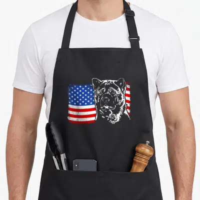Proud akita american flag apron - Grey Akita head silhouette overlapping a distressed red white and blue American flag — shown on a black cotton canvas apron against a white background