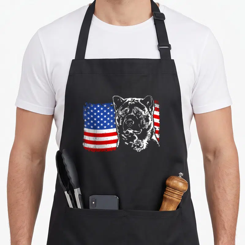 Proud akita american flag apron - Grey Akita head silhouette overlapping a distressed red white and blue American flag — shown on a black cotton canvas apron against a white background