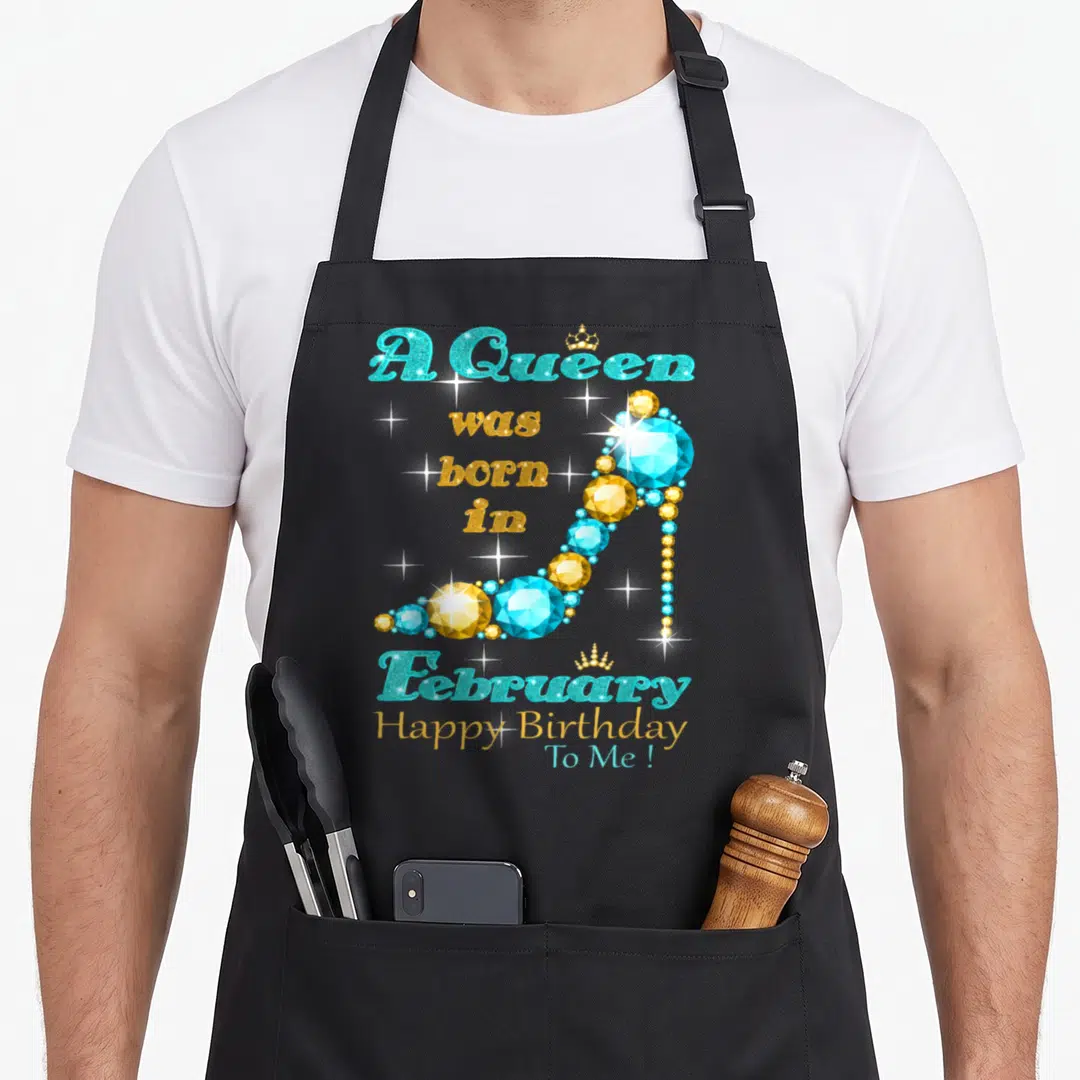 February baking queen apron - A Queen was born in February Happy Birthday To Me text with diamond high heel shoe — shown on a black cotton canvas apron against a white background