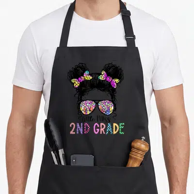 2nd grade tie-dye apron - Cartoon girl with space buns, leopard sunglasses reflecting crayons, and Little Miss 2nd — shown on a black cotton canvas apron against a white background