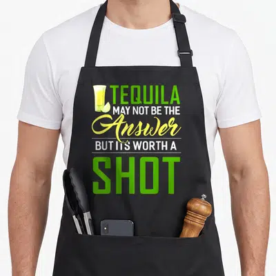 But tequila apron - Stacked text TEQUILA MAY NOT BE THE ANSWER BUT ITS WORTH A SHOT with shot glass and lime slice — shown on a black cotton canvas apron against a white background