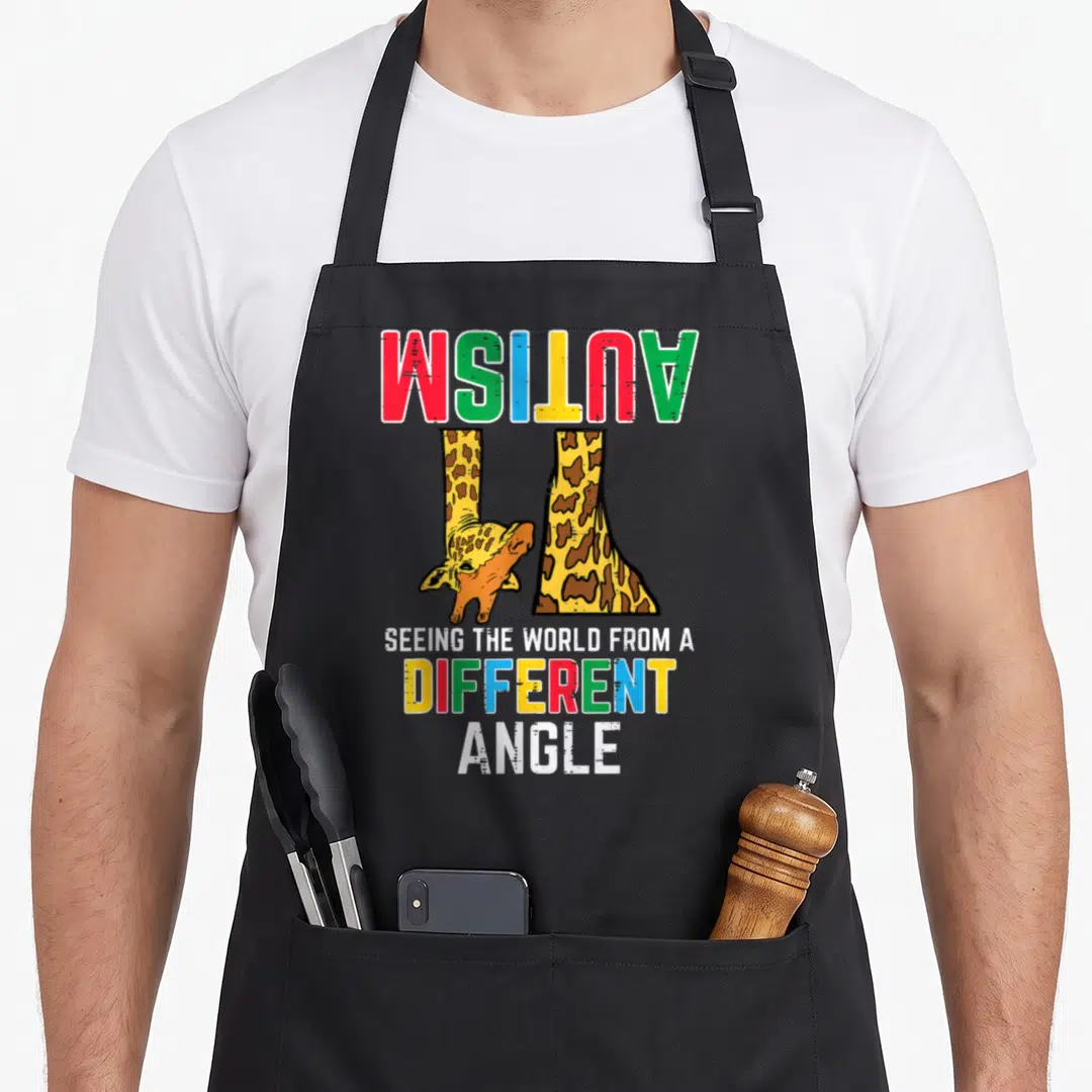 Autism giraffe apron - Upside down giraffe with inverted rainbow text reading autism and seeing the world — shown on a black cotton canvas apron against a white background