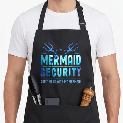 Mess mermaid apron - Blue watercolor text reading MERMAID SECURITY with two tridents and stars above — shown on a black cotton canvas apron against a white background