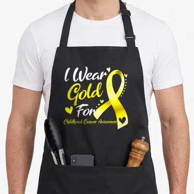 Funny childhood cancer awareness apron - Yellow awareness ribbon with small hearts and stacked text reading I Wear Gold — shown on a black cotton canvas apron against a white background