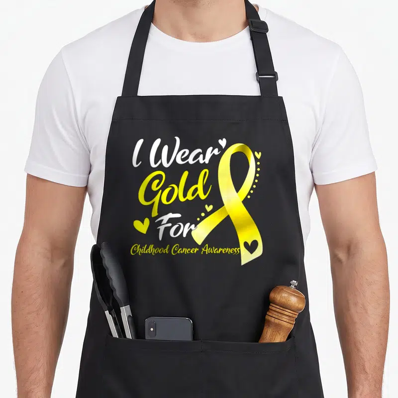 Funny childhood cancer awareness apron - Yellow awareness ribbon with small hearts and stacked text reading I Wear Gold — shown on a black cotton canvas apron against a white background