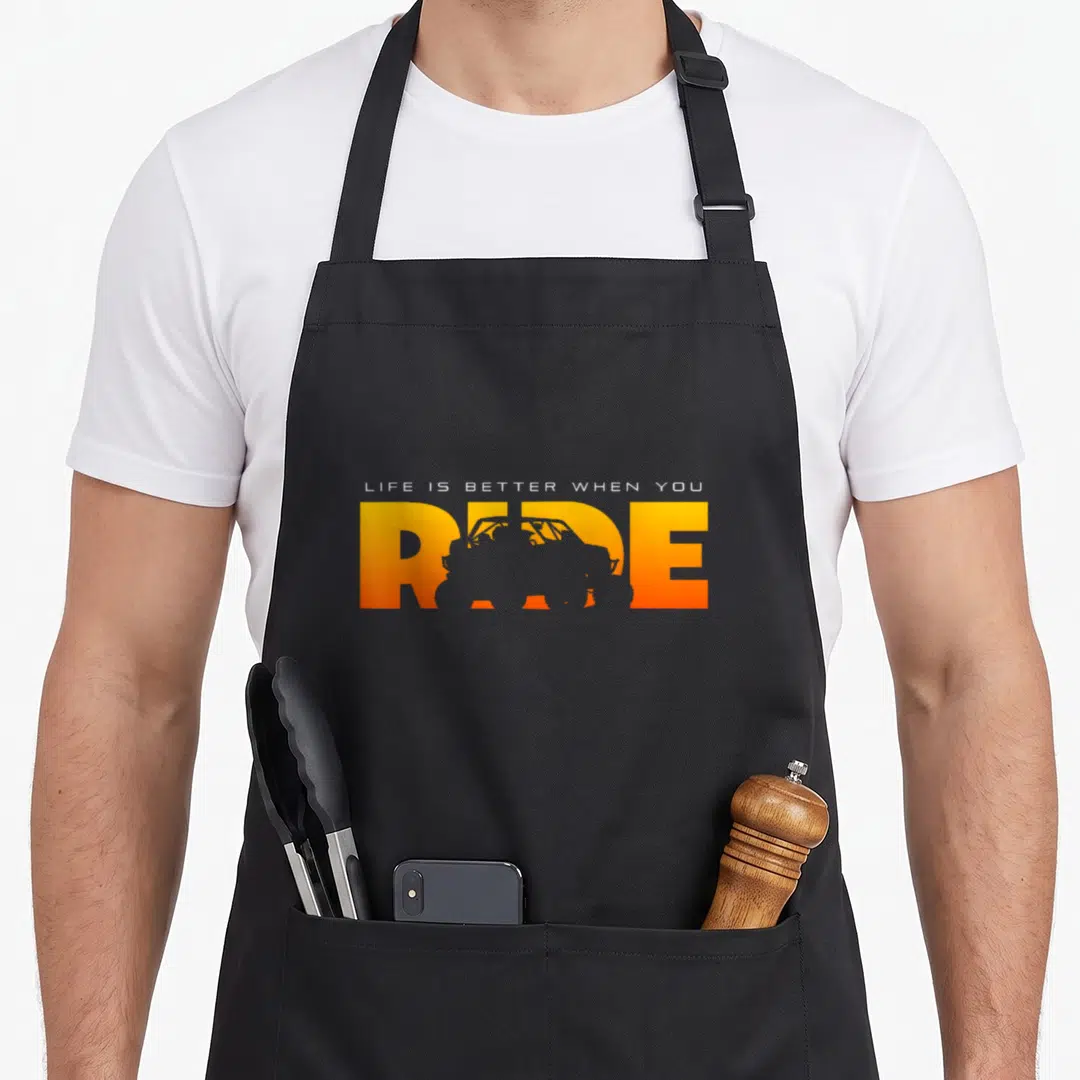 Quad atv road apron - LIFE IS BETTER WHEN YOU RIDE text with orange gradient and vehicle silhouette inside letters — shown on a black cotton canvas apron against a white background