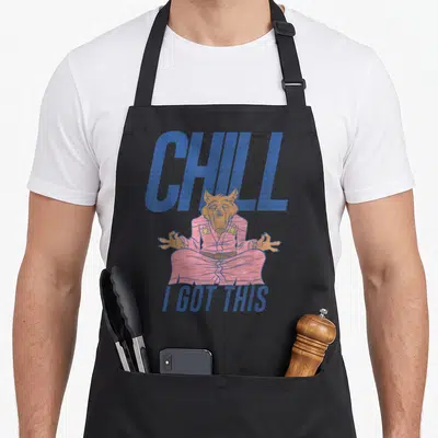 Chill master apron - Meditating wolf in pink robe with blue CHILL I GOT THIS text — shown on a black cotton canvas apron against a white background