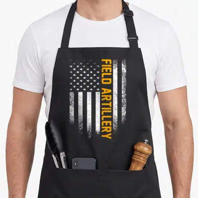 Field american flag apron - Vertical orange FIELD ARTILLERY text over distressed white USA flag stripes — shown on a black cotton canvas apron against a white background