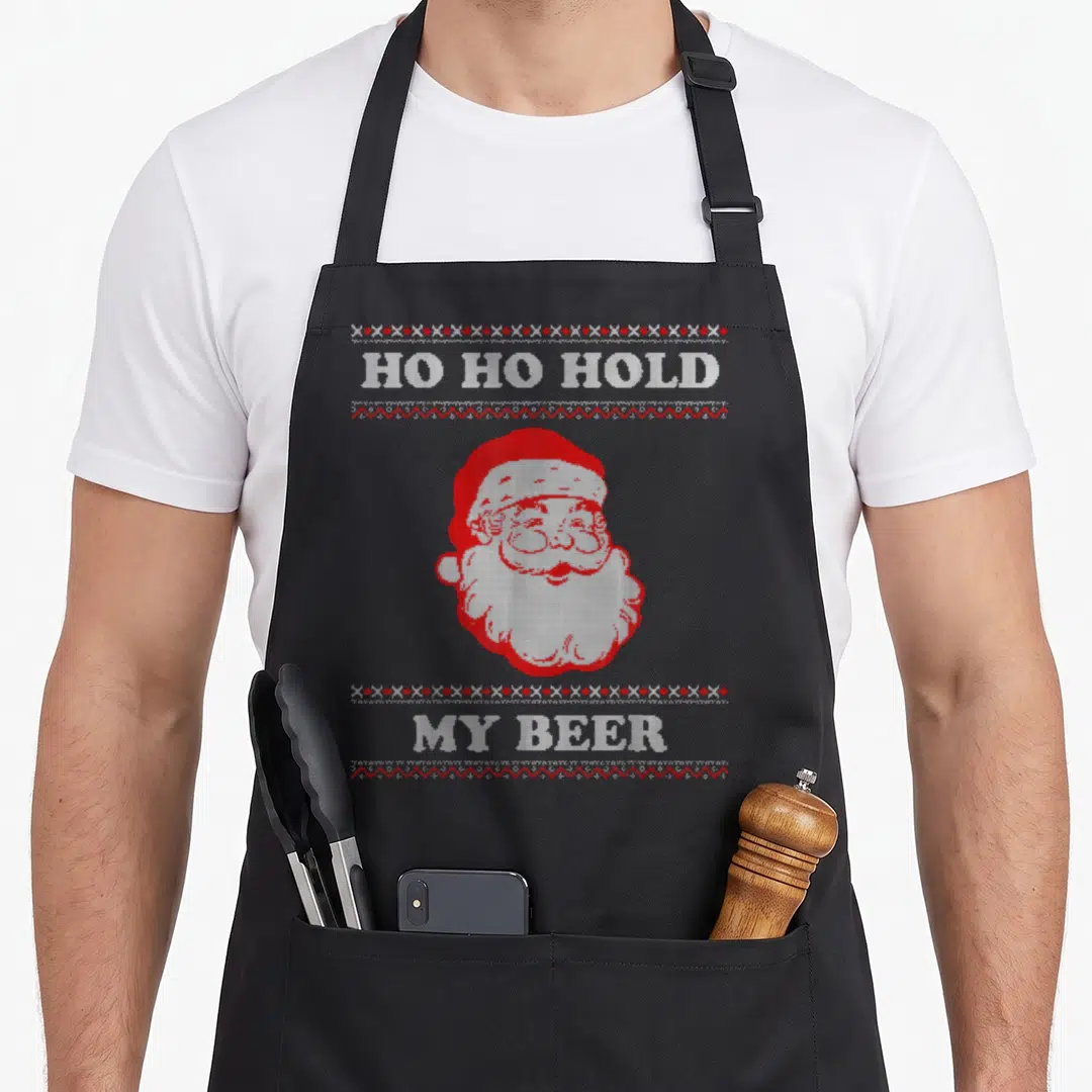 Hold ugly christmas apron - Pixelated red and white Santa face with text Ho Ho Hold My Beer and geometric borders — shown on a black cotton canvas apron against a white background