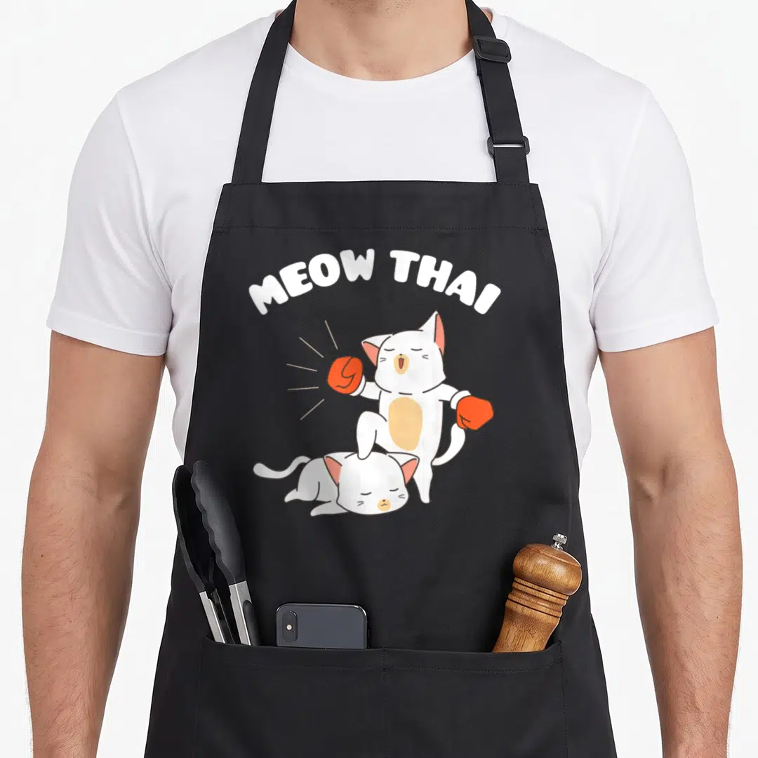 Thai cat apron - Cartoon white cats boxing with red gloves and MEOW THAI text arched above — shown on a black cotton canvas apron against a white background