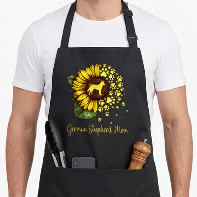 Sunflower mother's day aprons - Sunflower with dog silhouette and yellow paw prints above German Shepherd Mom script — shown on a black cotton canvas apron against a white background