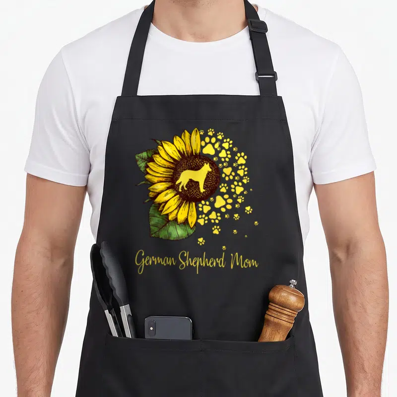Sunflower mother's day aprons - Sunflower with dog silhouette and yellow paw prints above German Shepherd Mom script — shown on a black cotton canvas apron against a white background