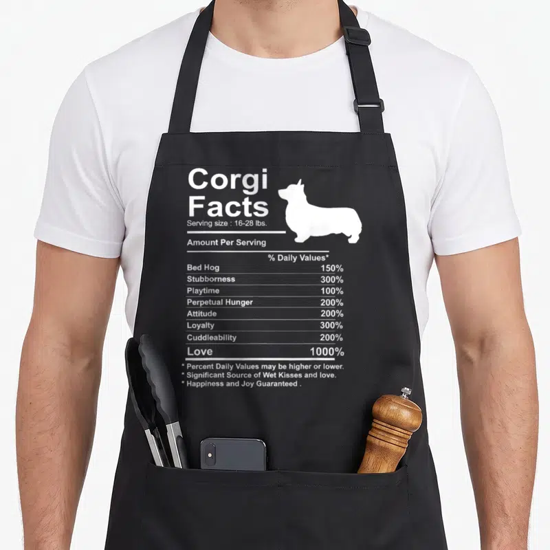 Fact corgi apron - White corgi silhouette and nutrition facts label listing love and stubbornness percentages — shown on a black cotton canvas apron against a white background
