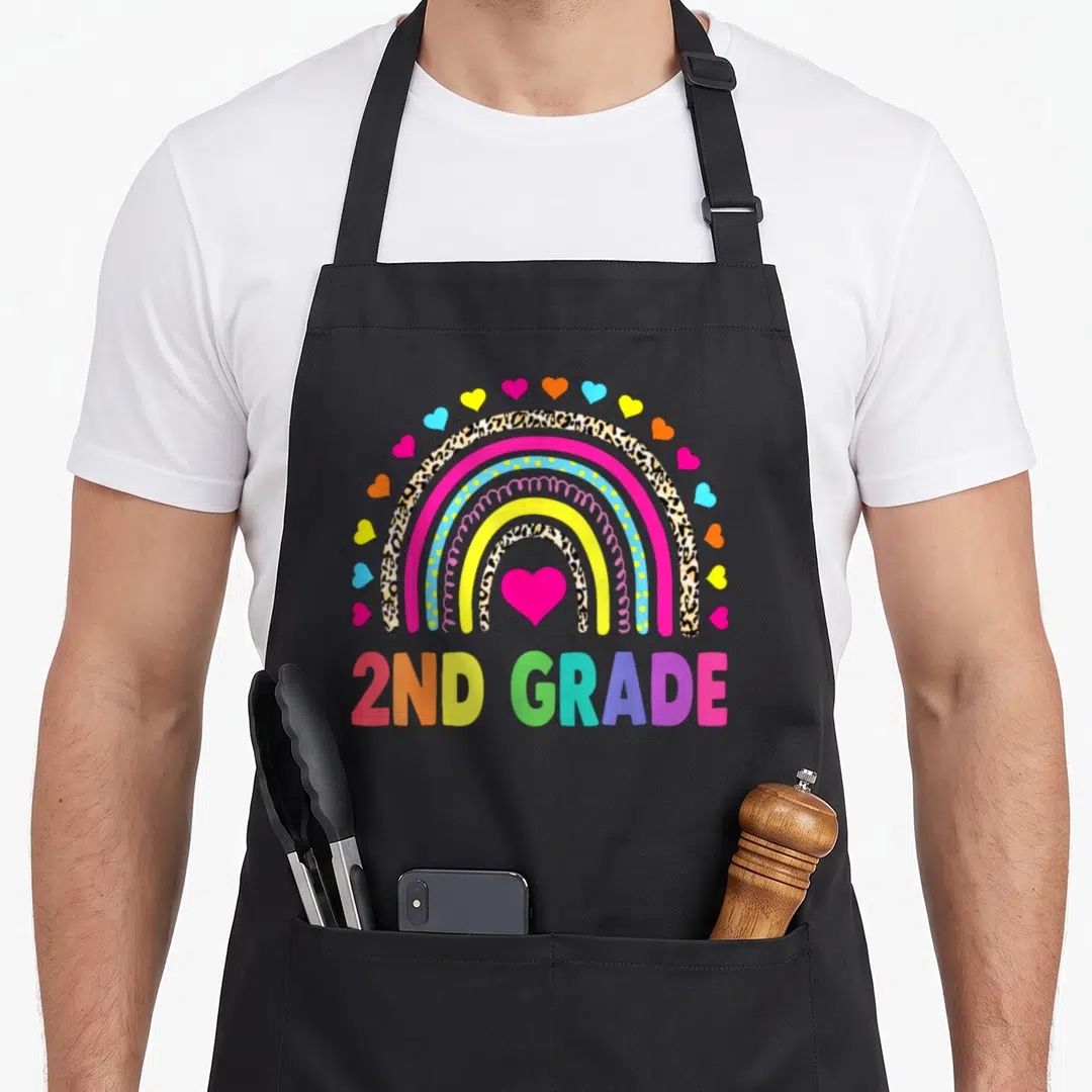 Rainbow teacher apron - Cartoon rainbow with leopard stripes and hearts above multicolored 2ND GRADE text — shown on a black cotton canvas apron against a white background