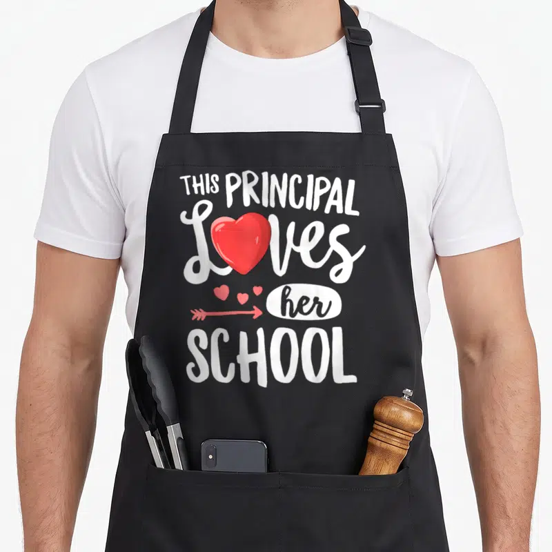 Principal valentine's day apron - White text This Principal Loves her School with red heart replacing O and arrow above — shown on a black cotton canvas apron against a white background