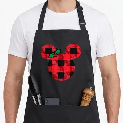 Icon christmas plaid apron - Mickey Mouse head silhouette filled with red black plaid and holly sprig — shown on a black cotton canvas apron against a white background