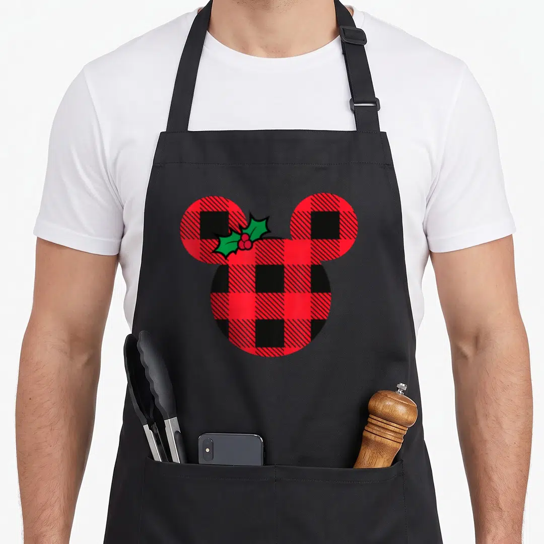 Icon christmas plaid apron - Mickey Mouse head silhouette filled with red black plaid and holly sprig — shown on a black cotton canvas apron against a white background