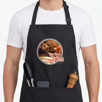 Vintage spaghetti lady and the tramp apron - Two dogs sharing a noodle in red white blue circle with You Had Me — shown on a black cotton canvas apron against a white background