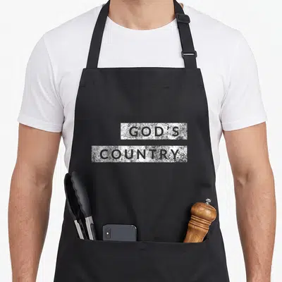 God country kitchen apron - Stacked distressed white blocks with grey text reading GOD'S COUNTRY — shown on a black cotton canvas apron against a white background