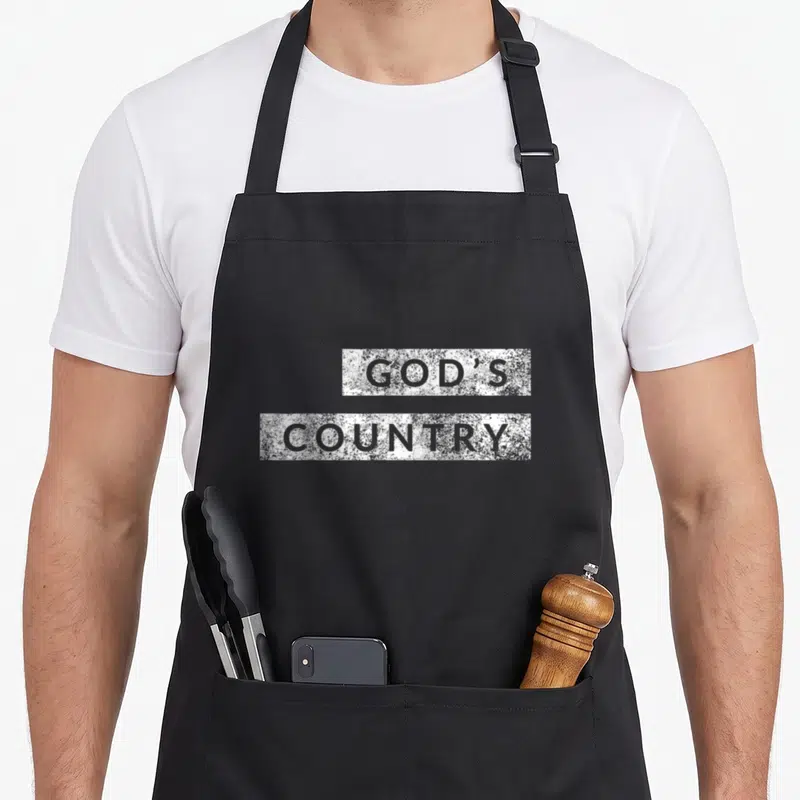 God country kitchen apron - Stacked distressed white blocks with grey text reading GOD'S COUNTRY — shown on a black cotton canvas apron against a white background