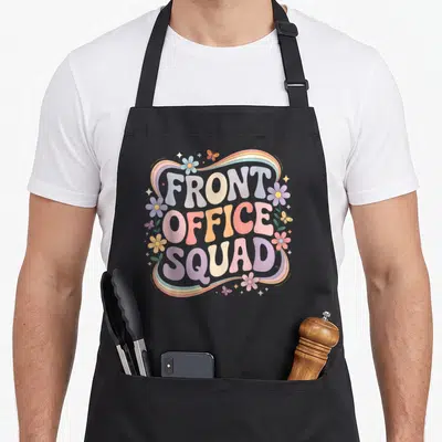 Squad admin office apron - Stacked FRONT OFFICE SQUAD text with rainbow border, flowers, and butterflies in pastel — shown on a black cotton canvas apron against a white background