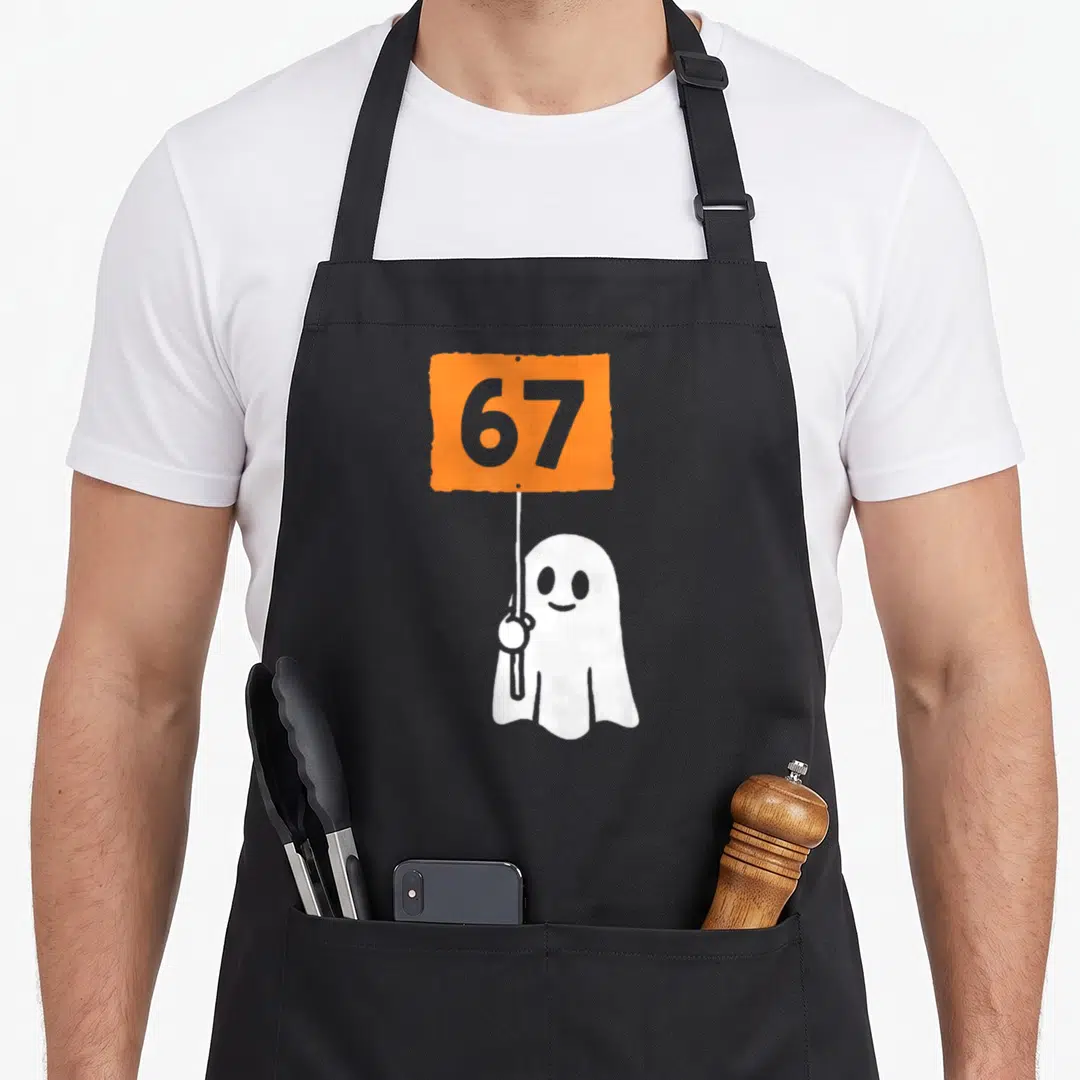 Six seven halloween apron - White cartoon ghost holding orange sign with grey number 67 on black fabric — shown on a black cotton canvas apron against a white background