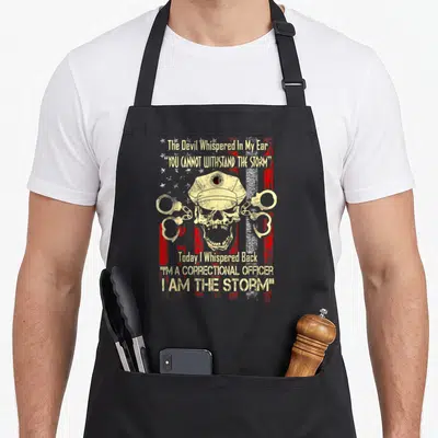 State line apron - Distressed skull in hat with crossed handcuffs and storm quote on striped background — shown on a black cotton canvas apron against a white background
