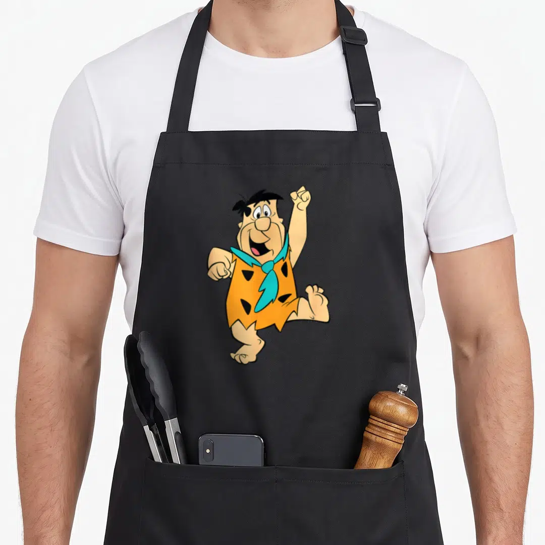 Solo flint apron - Fred Flintstone cartoon in orange tunic and blue tie centered on canvas — shown on a black cotton canvas apron against a white background