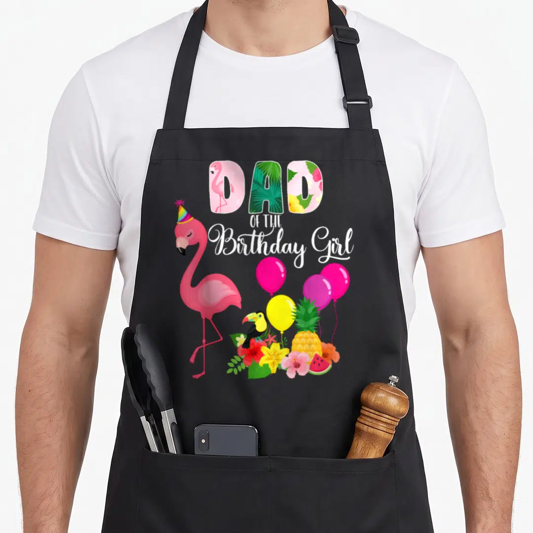 Funny birthday flamingo apron - Dad of the Birthday Girl text with cartoon flamingo, toucan, balloons, and tropical — shown on a black cotton canvas apron against a white background