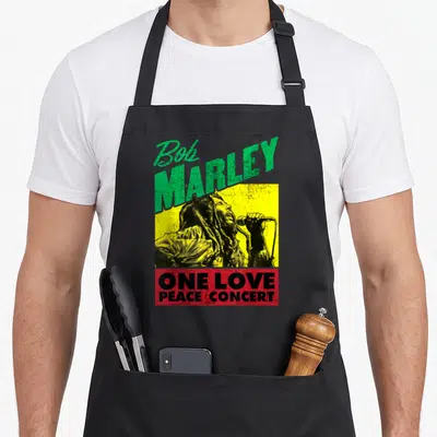 Bob concert apron - Distressed green Bob Marley text above yellow singer image and red One Love Peace Concert block — shown on a black cotton canvas apron against a white background