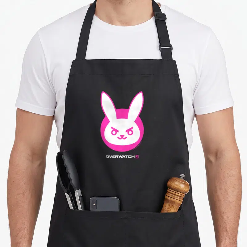 Centre rabbit apron - White rabbit head in pink circle with Overwatch 2 text below — shown on a black cotton canvas apron against a white background