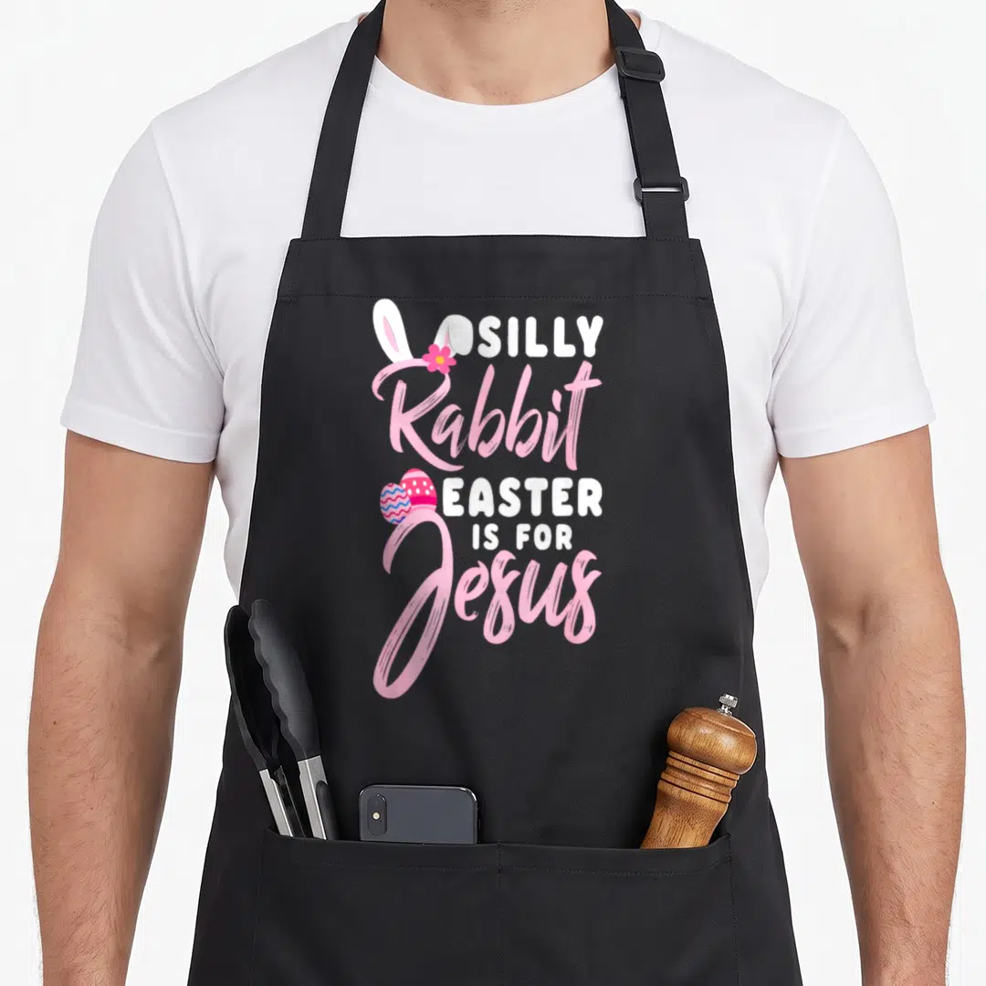 Easter rabbit apron - Stacked pink and white text reading Silly Rabbit Easter Is for Jesus with bunny ears and two eggs — shown on a black cotton canvas apron against a white background