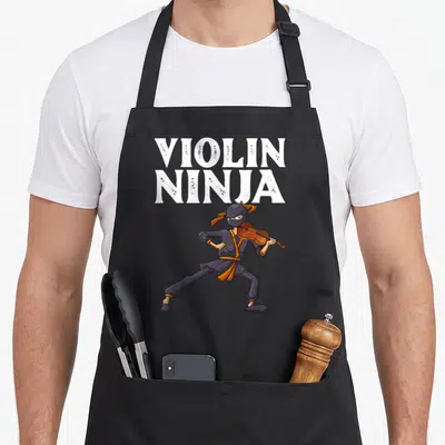 Ninja cello apron - Stacked white VIOLIN NINJA text above a cartoon ninja playing a violin in purple and orange — shown on a black cotton canvas apron against a white background