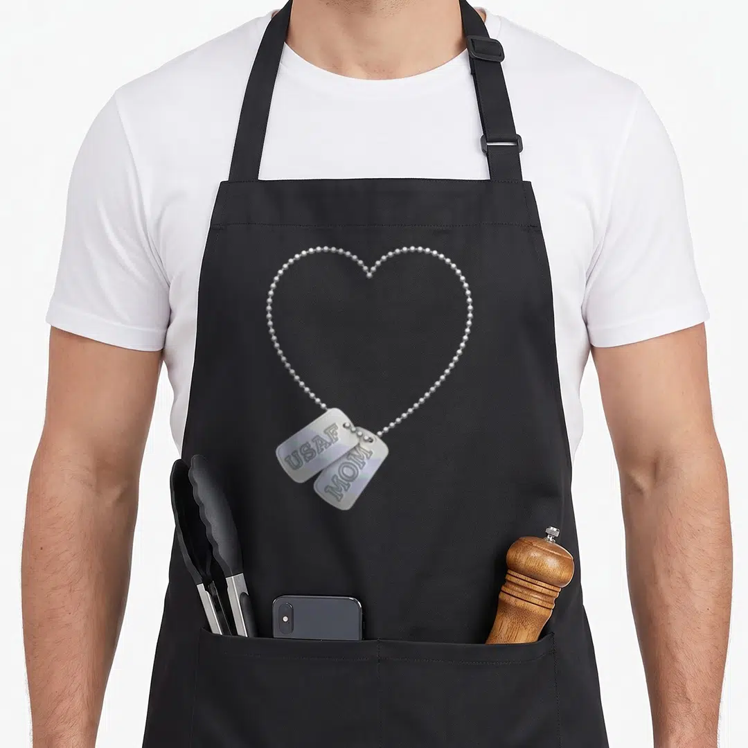 Tag dog apron - Realistic silver dog tags reading USAF and MOM on a heart-shaped chain — shown on a black cotton canvas apron against a white background