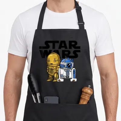 3po cartoon apron - Two small droids stand before STAR WARS text in cartoon style with black gold blue white colors — shown on a black cotton canvas apron against a white background