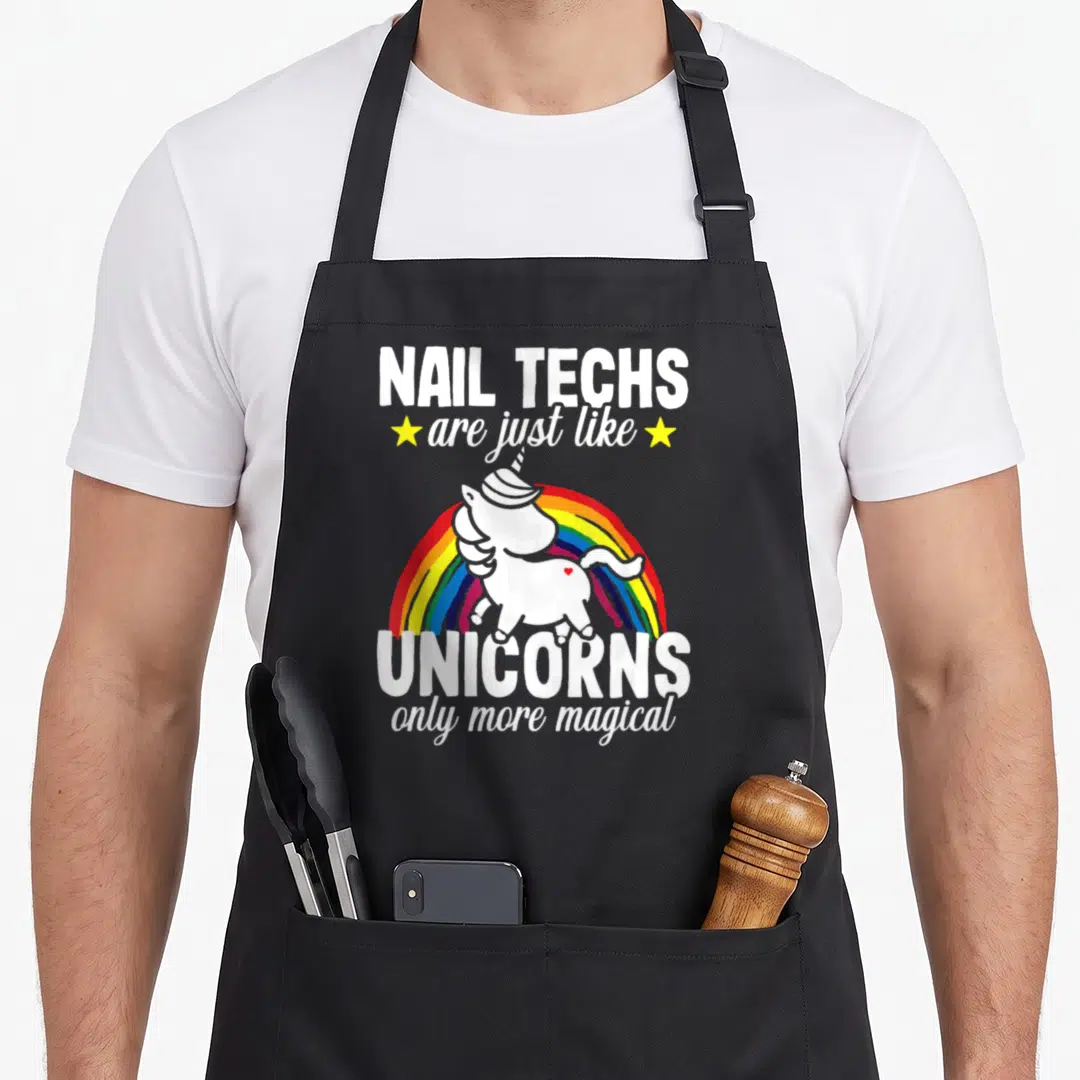 Unicorn manicurist apron - Nail techs unicorns text with rainbow and two stars — shown on a black cotton canvas apron against a white background