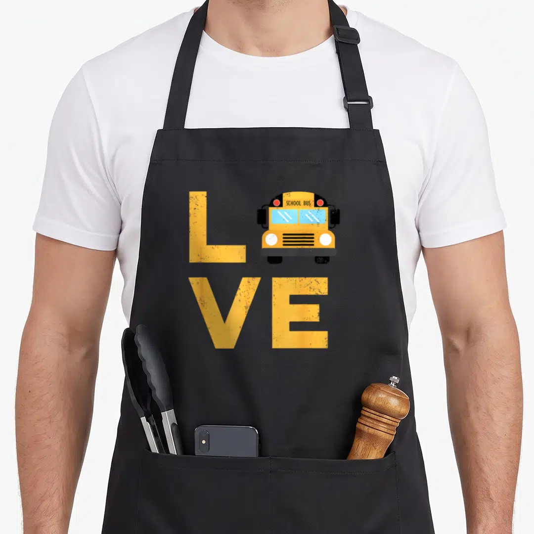 Typography omnibus apron - Cartoon school bus replaces letter O in yellow LOVE typography with black and blue accents — shown on a black cotton canvas apron against a white background